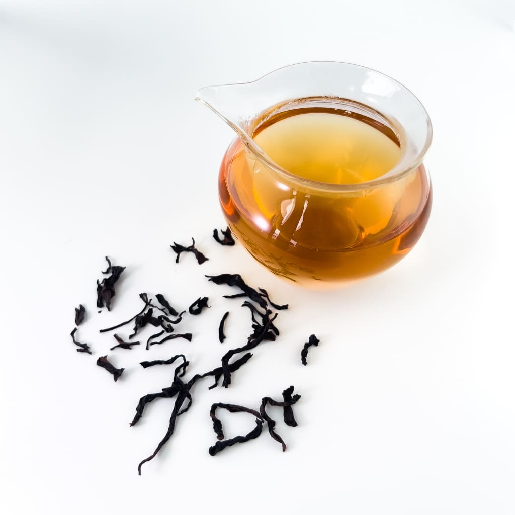 Glass cha hai with brewed tea and loose tea leaves on a white background